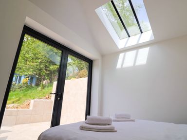 A bedroom with a skylight and glass doors opening to a garden with towels on the bed at Upper Cottage in Rocombe near Uplyme