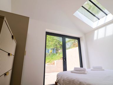 A bedroom with white bed linens folded towels on bed a chest of drawers and glass doors leading outside at Upper Cottage in Rocombe near Uplyme