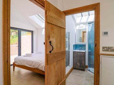 A bedroom with a wooden bed and white bedding next to a bathroom with a sink, mirror, and shower at Upper Cottage in Rocombe near Uplyme