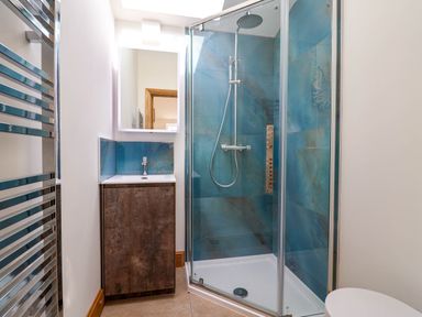 A bathroom with a glass shower enclosure a blue tiled wall a wooden vanity with sink and a metal towel rack at Upper Cottage in Rocombe near Uplyme
