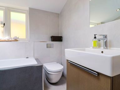 A bathroom with a bathtub, wall-mounted toilet, sink with a soap dispenser, and a window with decorative fish at Upper Cottage in Rocombe near Uplyme