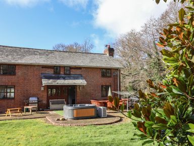 An outdoor patio area with a hot tub wooden bench table and chairs outside a brick house at Mill Cottage in Aylesbeare