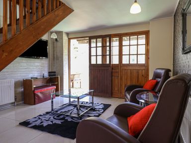 A living room with two armchairs with red cushions a glass coffee table and wooden doors at Mill Cottage in Aylesbeare