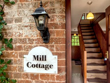A brick wall with a lamp and Mill Cottage sign next to a wooden staircase inside a house at Mill Cottage in Aylesbeare