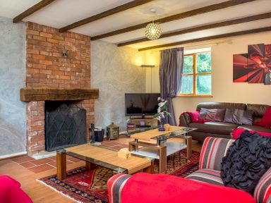 A living room with brick fireplace wooden beams glass coffee tables and striped armchair at Mill Cottage in Aylesbeare