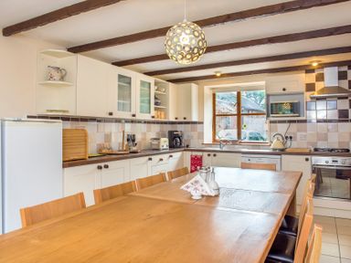 A kitchen with wooden dining table and chairs white cabinets and a refrigerator at Mill Cottage in Aylesbeare