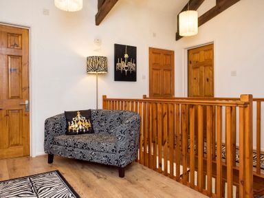 An upper hallway with wooden doors a patterned loveseat and wooden railing at Mill Cottage in Aylesbeare