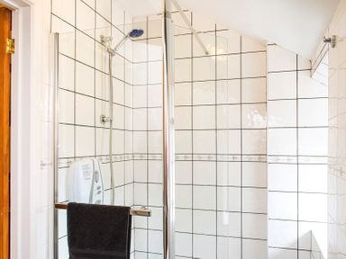 A tiled shower area with a glass door a black towel a showerhead and a soap dispenser at Mill Cottage in Aylesbeare