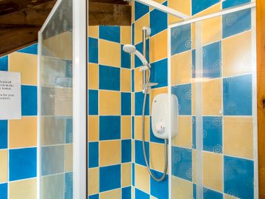 A shower with blue and yellow tiled walls and a wooden ceiling at Mill Cottage in Aylesbeare