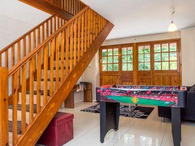 A room with wooden stairs a foosball table a small shelf with books and a sofa near wooden window doors at Mill Cottage in Aylesbeare