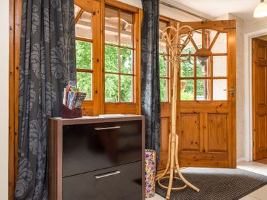 An entryway with wooden double doors a coat rack a black cabinet with magazines and dark patterned curtains at Mill Cottage in Aylesbeare