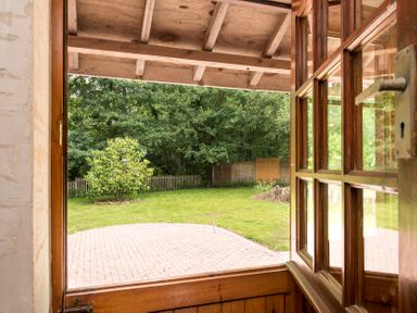 A wooden door open to a garden with a paved patio green grass a small tree and a wooden fence at Mill Cottage in Aylesbeare