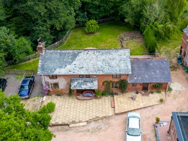 An aerial view of a brick house with a tiled roof driveway cars and a fenced garden at Mill Cottage in Aylesbeare