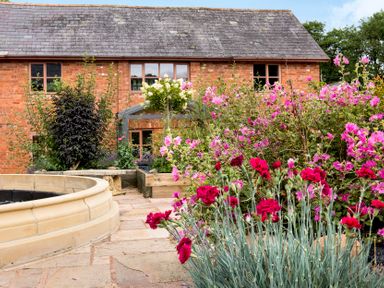 A garden with red and pink flowers and a brick house in the background at Mill Cottage in Aylesbeare