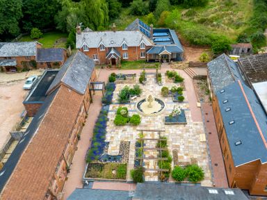 An aerial view of a courtyard with a central fountain and garden beds surrounded by four brick buildings at Mill Cottage in Aylesbeare