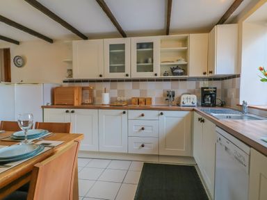 A kitchen with white cabinets wooden countertops a dining table with plates and glasses and kitchen appliances at Mill Cottage in Aylesbeare