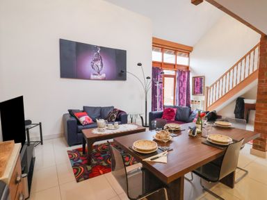A living room with two sofas a coffee table dining table set with plates and glasses and a staircase at Cob Barn in Aylesbeare