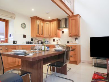A kitchen with wooden cabinets a dining table set with plates glasses and cutlery and a television on a stand at Cob Barn in Aylesbeare