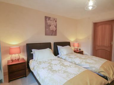 A bedroom with two single beds nightstands with lamps and a painting above the beds at Cob Barn in Aylesbeare