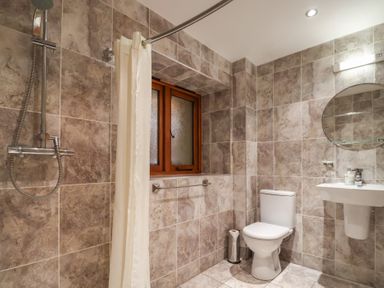A bathroom with a shower, toilet, sink, and a window at Cob Barn in Aylesbeare
