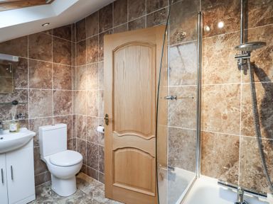 A bathroom with a toilet a sink with cabinet a wooden door and a bathtub with shower at Cob Barn in Aylesbeare