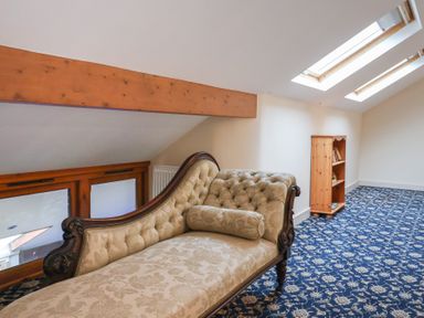 A room with a patterned carpet a wooden bookshelf and a vintage upholstered chaise longue under skylight windows at Cob Barn in Aylesbeare