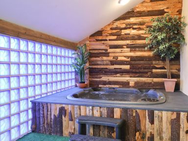 An indoor hot tub with wood paneling around it and two potted plants beside it at Cob Barn in Aylesbeare