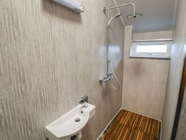 A bathroom with a wall-mounted sink and a shower area with wooden slatted flooring at Cob Barn in Aylesbeare