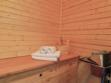 An interior of a wooden sauna with towels and a bucket with ladles on a bench and a sauna heater with stones