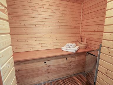 A wooden sauna room with towels and a bucket on a bench at Cob Barn in Aylesbeare