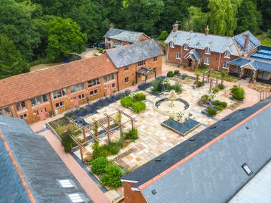 A courtyard with a central fountain surrounded by plants and wooden pergolas between brick buildings at Cob Barn in Aylesbeare