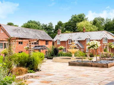 A courtyard with garden beds and a fountain in front of brick houses at Cob Barn in Aylesbeare