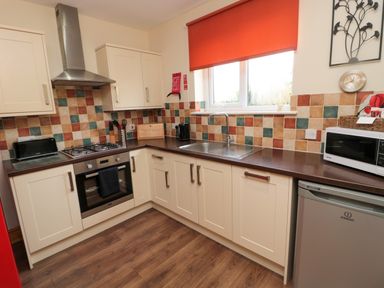 A kitchen with cream cabinets a gas stove an oven a toaster a microwave and a sink under a window at Stable Cottage in Cottonshopeburnfoot near Otterburn