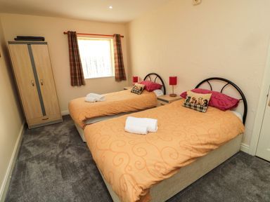 A bedroom with two single beds with orange bedspreads and a wooden wardrobe at Stable Cottage in Cottonshopeburnfoot near Otterburn