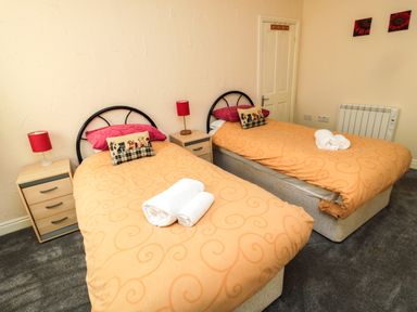 A bedroom with two single beds orange bedding and red lamps at Stable Cottage Cottonshopeburnfoot near Otterburn