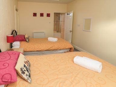A bedroom with two single beds orange bedspreads and a door leading to a bathroom at Stable Cottage in Cottonshopeburnfoot near Otterburn