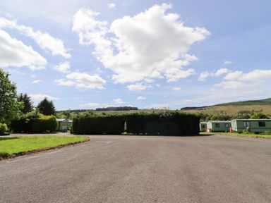 An outdoor area with grass, trees, clouds and caravans at Stable Cottage Cottonshopeburnfoot near Otterburn