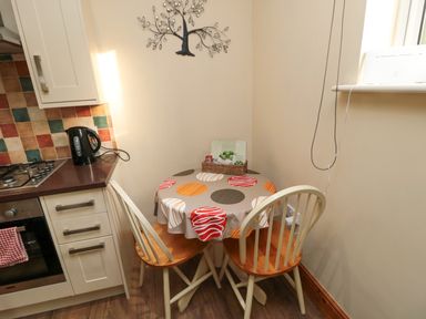 A kitchen corner with a small round table covered with a patterned cloth and two wooden chairs at Fir Tree Cottage Cottonshopeburnfoot near Otterburn