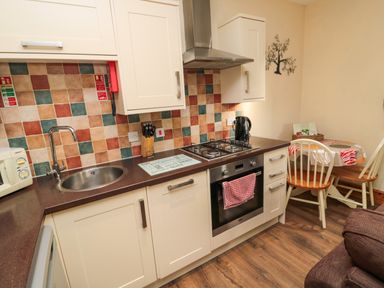 A kitchen with a sink microwave knives stove oven and a small dining table with chairs at Fir Tree Cottage Cottonshopeburnfoot near Otterburn