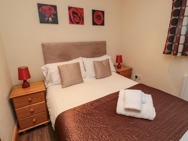A bedroom with a double bed two bedside tables with lamps and rose paintings on the wall at Fir Tree Cottage in Cottonshopeburnfoot near Otterburn