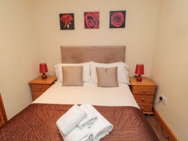 A bedroom with a double bed two bedside tables with red lamps and rose paintings above the bed at Fir Tree Cottage in Cottonshopeburnfoot near Otterburn