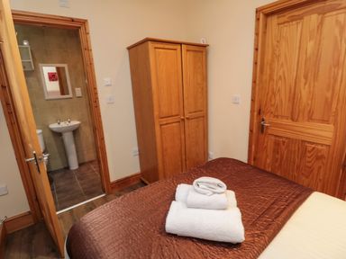 A bedroom with a bed, folded towels on the bed, a wooden wardrobe, and an open door leading to a bathroom at Fir Tree Cottage in Cottonshopeburnfoot near Otterburn