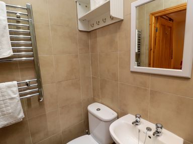 A bathroom with beige tiles a white toilet a white sink with two taps a towel rack with white towels and a mirror at Fir Tree Cottage Cottonshopeburnfoot near Otterburn