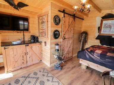 A wooden cabin room with a bed a flat screen tv a wooden cabinet a glass table with an eagle sculpture and a rusty door at Whiskey Creek Cabin in Castlerock