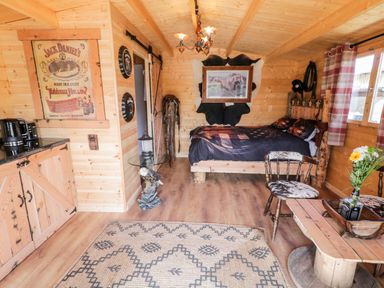 A wooden cabin interior with a bed a chair and a coffee table near a window at Whiskey Creek Cabin in Castlerock