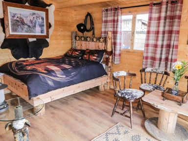 A wooden bedroom with a bed a round glass table two chairs and a wooden spool table at Whiskey Creek Cabin in Castlerock