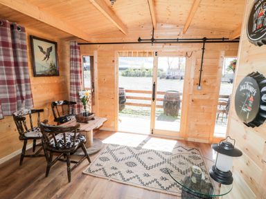 A wooden cabin interior with three chairs around a wooden table a rug glass table with a lantern and sliding glass doors at Whiskey Creek Cabin in Castlerock