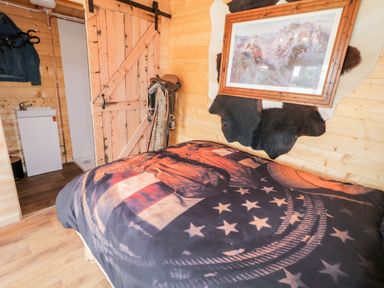 A bedroom with a bed covered in a blanket with a horse design wooden walls a saddle and a barn style door at Whiskey Creek Cabin in Castlerock