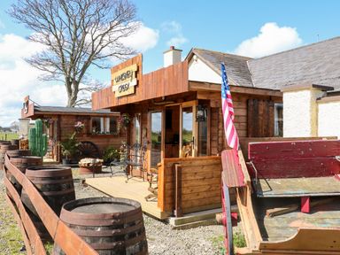 A wooden cabin with barrels and an american flag outside at Whiskey Creek Cabin in Castlerock