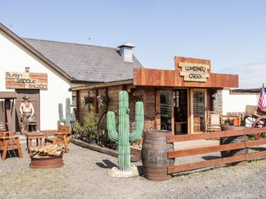 An outdoor area with wooden chairs fire pit cactus and wooden building with signs at Whiskey Creek in Castlerock